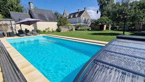 A swimming pool with lounge chairs and a covered area, surrounded by a well-maintained lawn and stone buildings. - Gîte with swimming pool, Nordic bath, close to the landing beaches (le manoir)