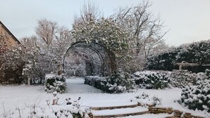 Un jardín cubierto de nieve con un camino de piedra que conduce a una estructura arqueada.