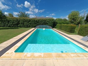 Una piscina rettangolare con bordo piastrellato, circondata da un prato curato e siepi.
