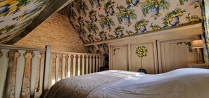 A bedroom with a sloped ceiling, a bed with a white bedspread, a wooden headboard, and a wall with a lemon and plant wallpaper.