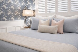 A bedroom with a bed, pillows, a lamp, and a wall with floral wallpaper.