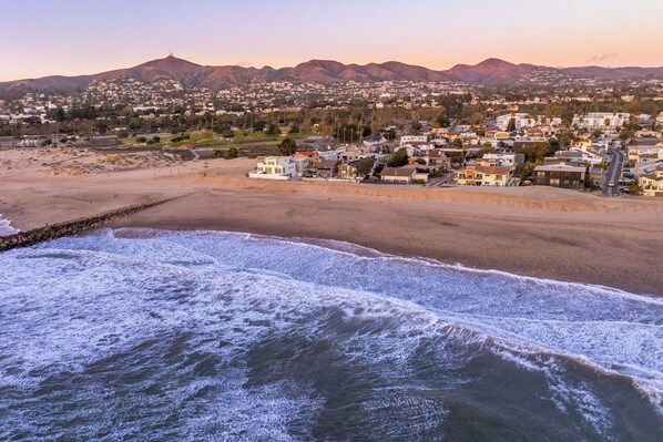 A coastal town with a beach, houses, and mountains in the background.