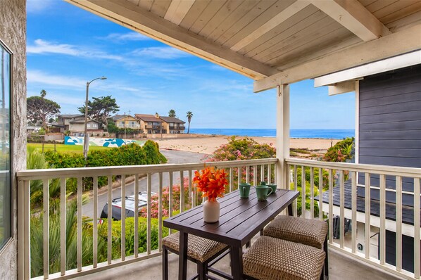 Un balcón con vista a la playa, una mesa con sillas y un jarrón con flores.