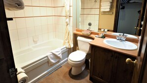 A bathroom with a bathtub, toilet, and sink. - Apex Inn 223 sleeps 5. Ski in/Ski out. Steps to Apex Resort Village (Penticton)