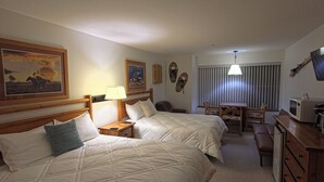 A hotel room with two beds, a desk, a chair, a lamp, a painting, and a ceiling light. - Apex Inn 223 sleeps 5. Ski in/Ski out. Steps to Apex Resort Village (Penticton)