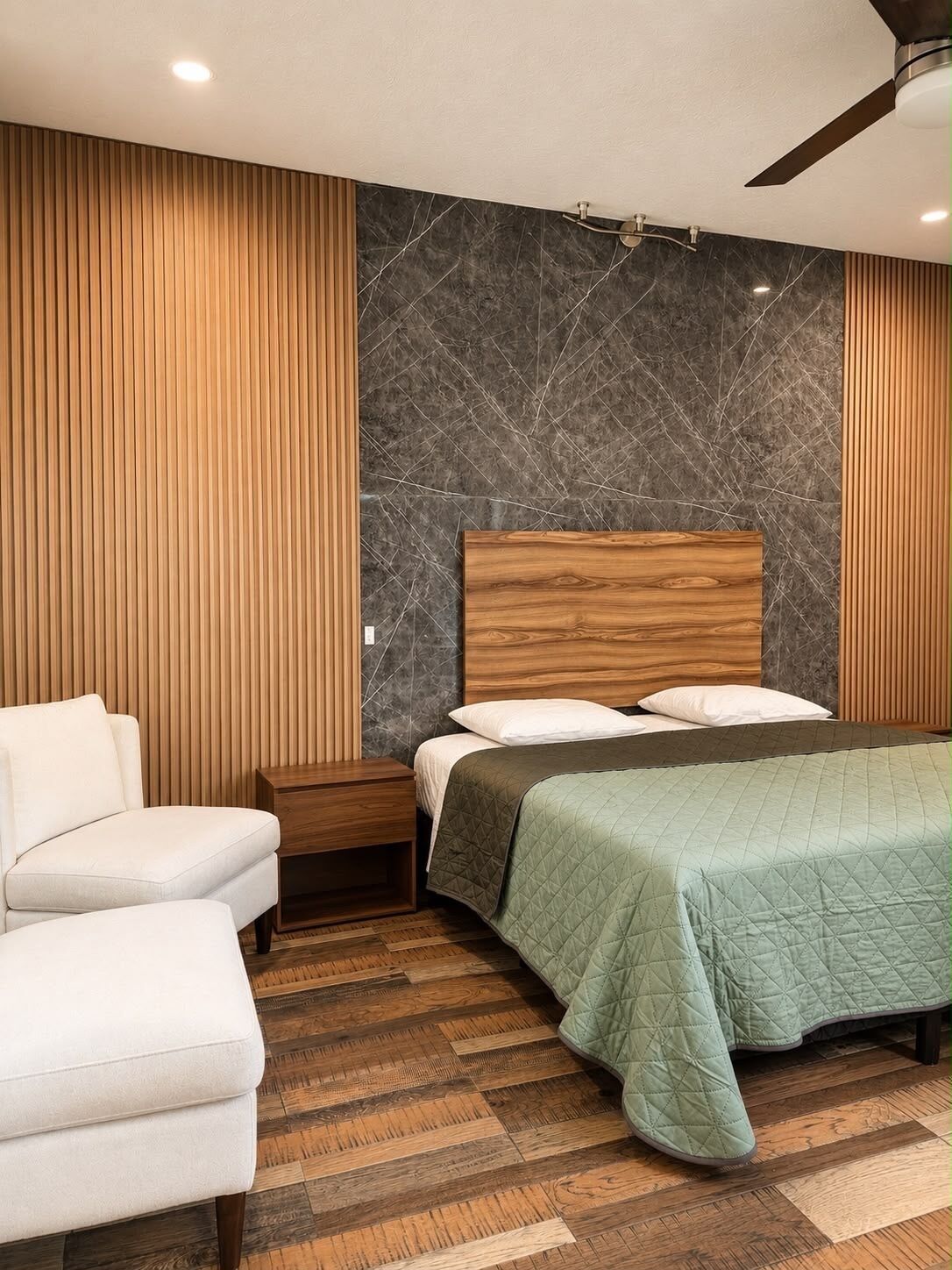 A bedroom with a bed, a nightstand, a chair, and a ceiling fan.