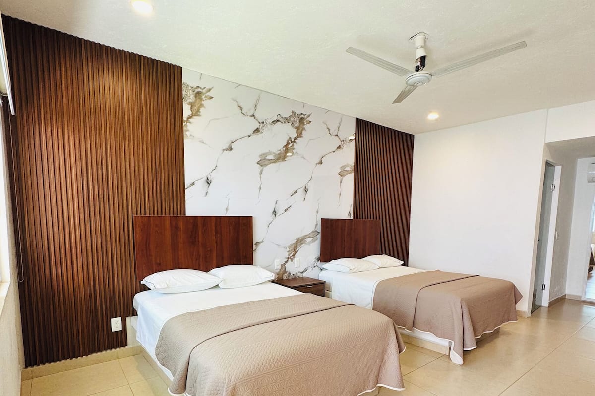 Habitación de hotel con dos camas, un ventilador de techo y una pared con diseño de mármol.