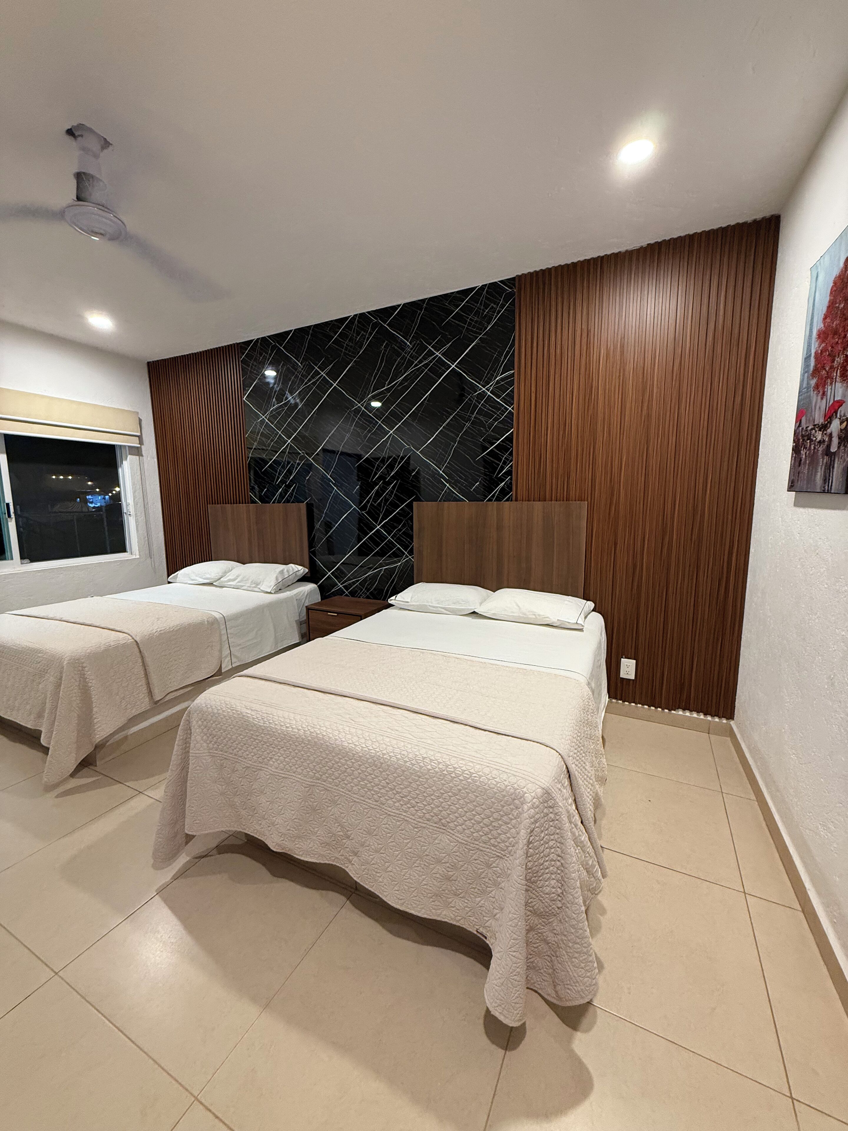 Habitación de hotel con dos camas, un gran panel de pared negro decorativo, paneles de madera y un cuadro en la pared.