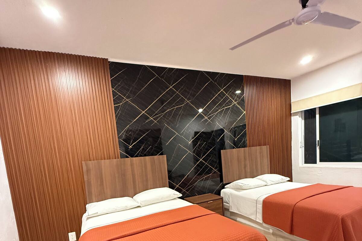 Una habitación de hotel moderna con dos camas, un ventanal grande y un panel decorativo en la pared.