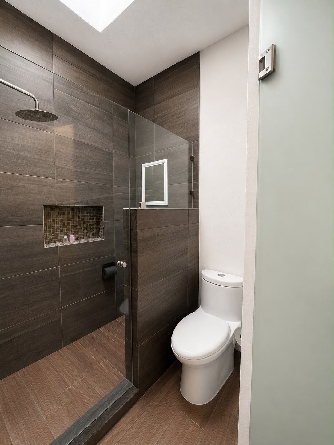 A modern bathroom with a shower, toilet, and a small window.