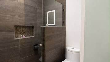 A modern bathroom with a shower, toilet, and a small window.