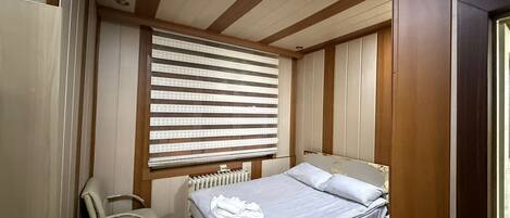A bedroom with a bed, a chair, a radiator, and a window with blinds.