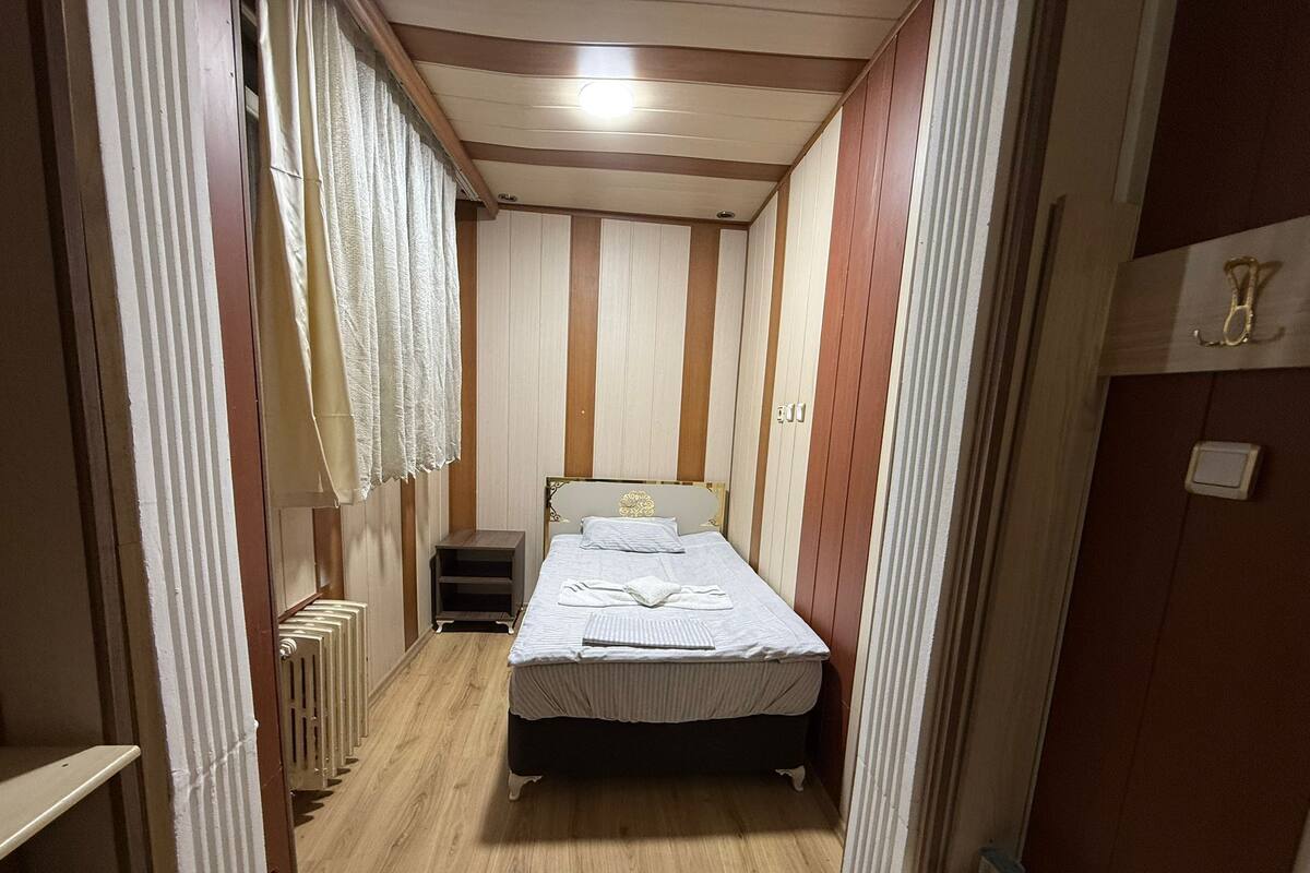 A narrow room with a bed, a small nightstand, and a radiator.