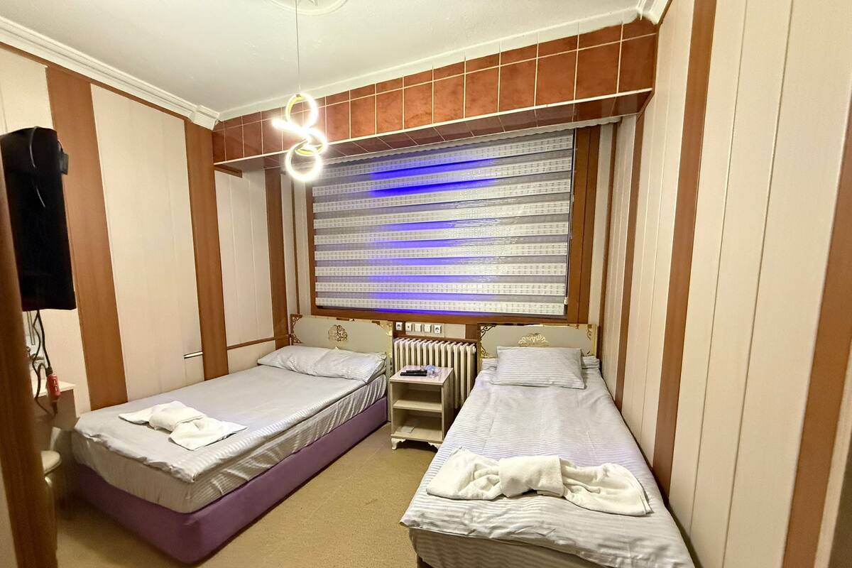 A small, compact room with two single beds, a radiator, and a window with a blue light.