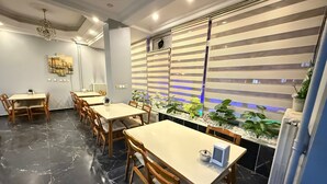 A modern dining area with marble flooring, wooden tables and chairs, and a decorative wall with plants and a blue-lit window. - Otel Büyük Doğu  (Erzurum)