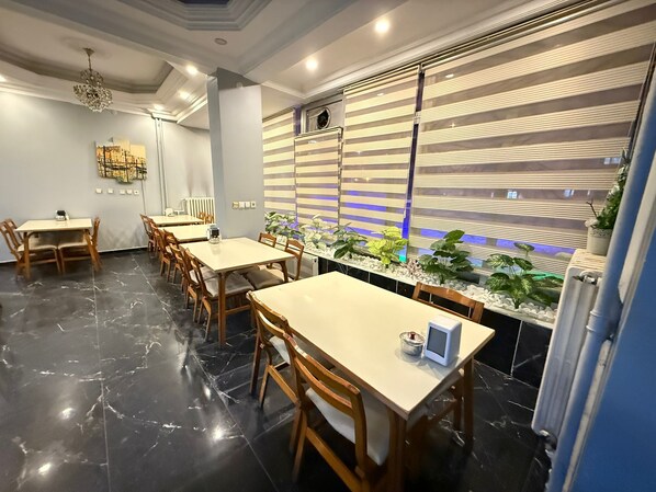 A modern dining area with marble flooring, wooden tables and chairs, and a decorative wall with plants and a blue-lit window. - Otel Büyük Doğu  (Erzurum)