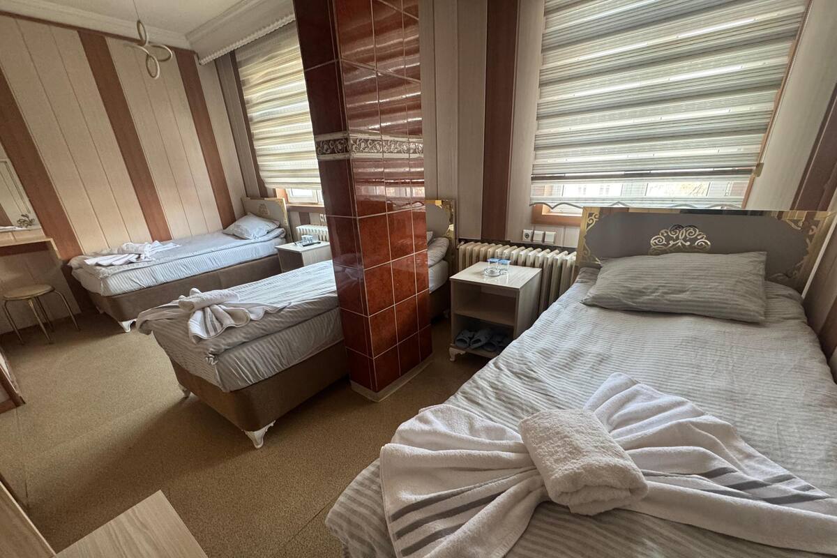 A hotel room with two single beds, a large bed, a wooden column, a radiator, and a small table with a glass.