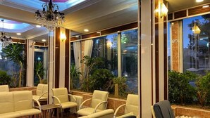 A well-lit indoor seating area with leather chairs and a chandelier, large windows with a view of greenery, and a tiled floor. - Otel Büyük Doğu  (Erzurum)
