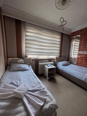 A hotel room with two single beds, a radiator, a small table with a glass, and a window with blinds. - Otel Büyük Doğu  (Erzurum)