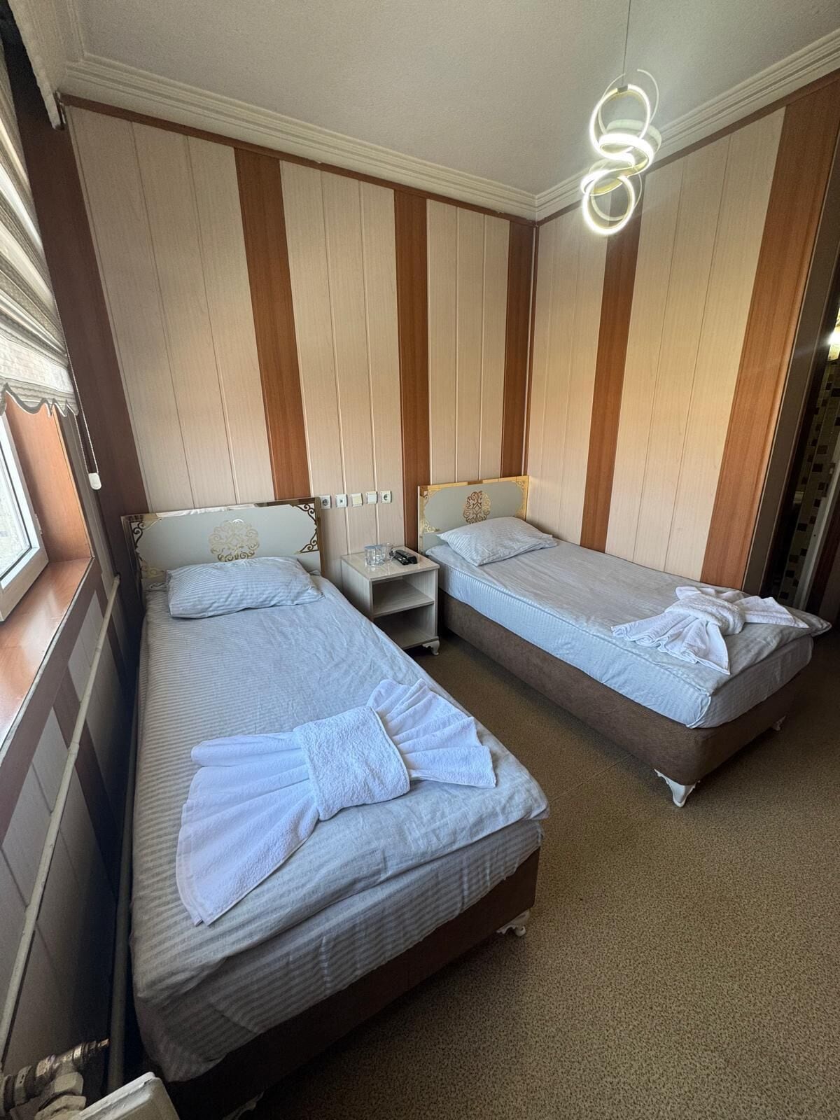 A hotel room with two beds, a nightstand, and a modern light fixture.