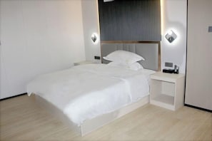 A modern hotel room with a neatly made bed, bedside tables, and wall-mounted lighting. - Huilong Hotel (Sihui)