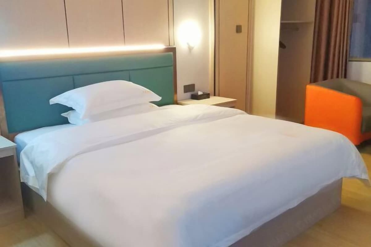 A hotel room with a large bed, a nightstand, a bedside table, and a wardrobe.