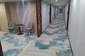 A hotel corridor with a patterned carpet, two chairs, a small round table, and a decorative screen. - Huilong Hotel (Sihui)