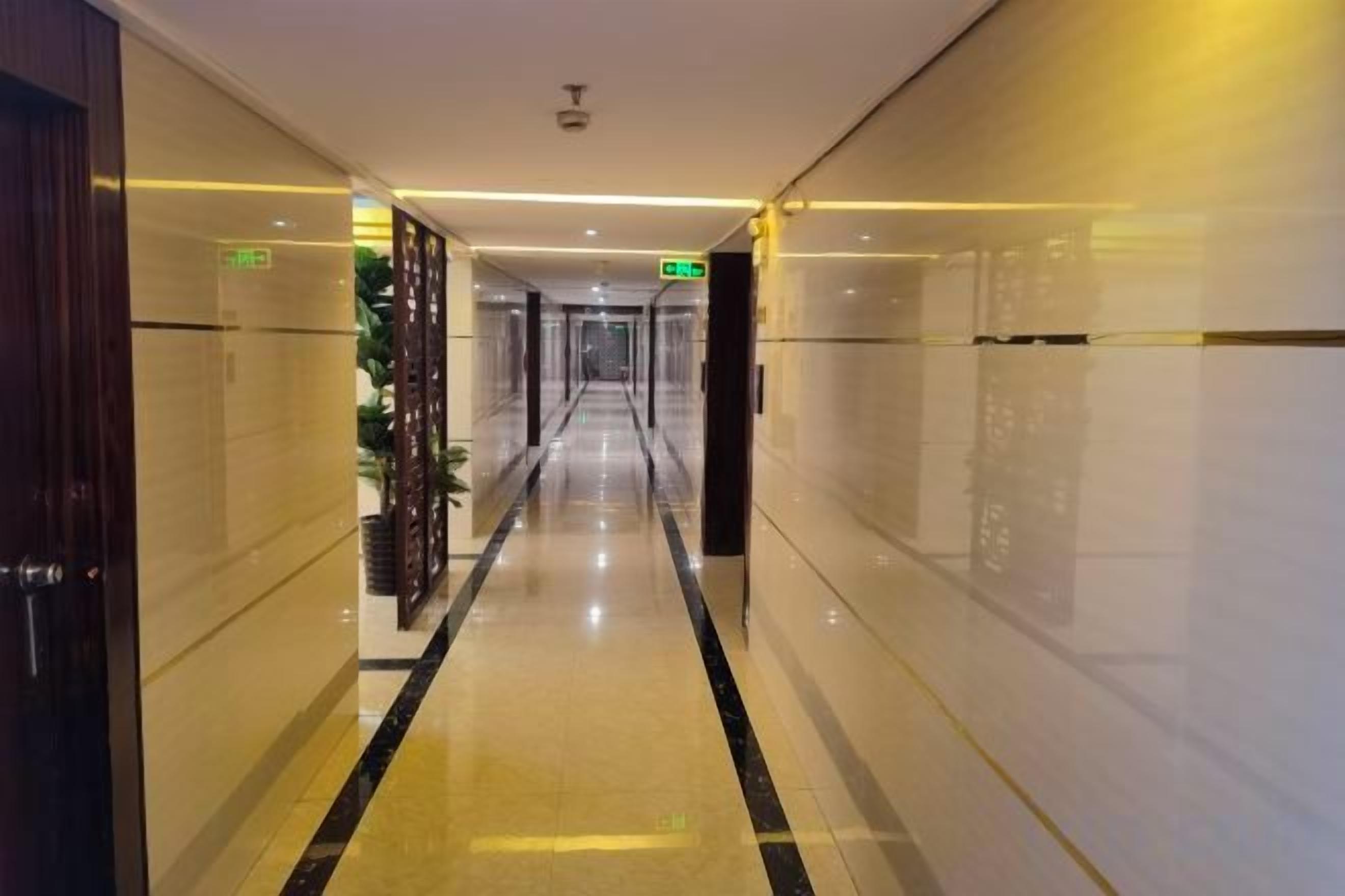 A hotel corridor with a shiny floor, doors on both sides, and a green exit sign.