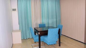 A dining area with a glass-top table and four blue chairs, a white cabinet, and a curtain with a vertical striped pattern.