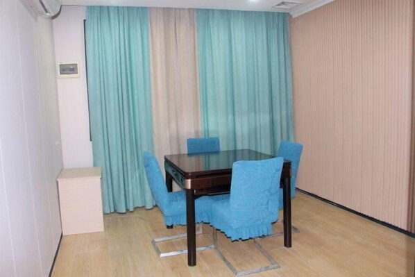 A dining area with a glass-top table and four blue chairs, a white cabinet, and a curtain with a vertical striped pattern. - Huilong Hotel (Sihui)