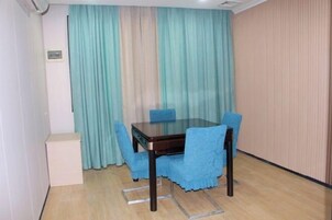 Un comedor con una mesa de vidrio y cuatro sillas azules, un armario blanco y una cortina con estampado de rayas verticales.