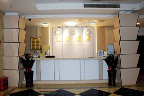 A hotel reception desk with a clock, a framed welcome sign, and a potted plant. - Huilong Hotel (Sihui)