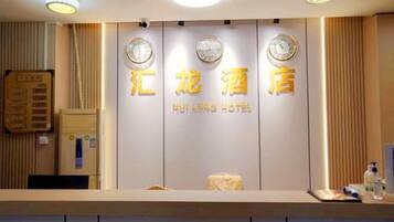 A hotel reception desk with a clock, a sign with hotel name, and a reception counter.