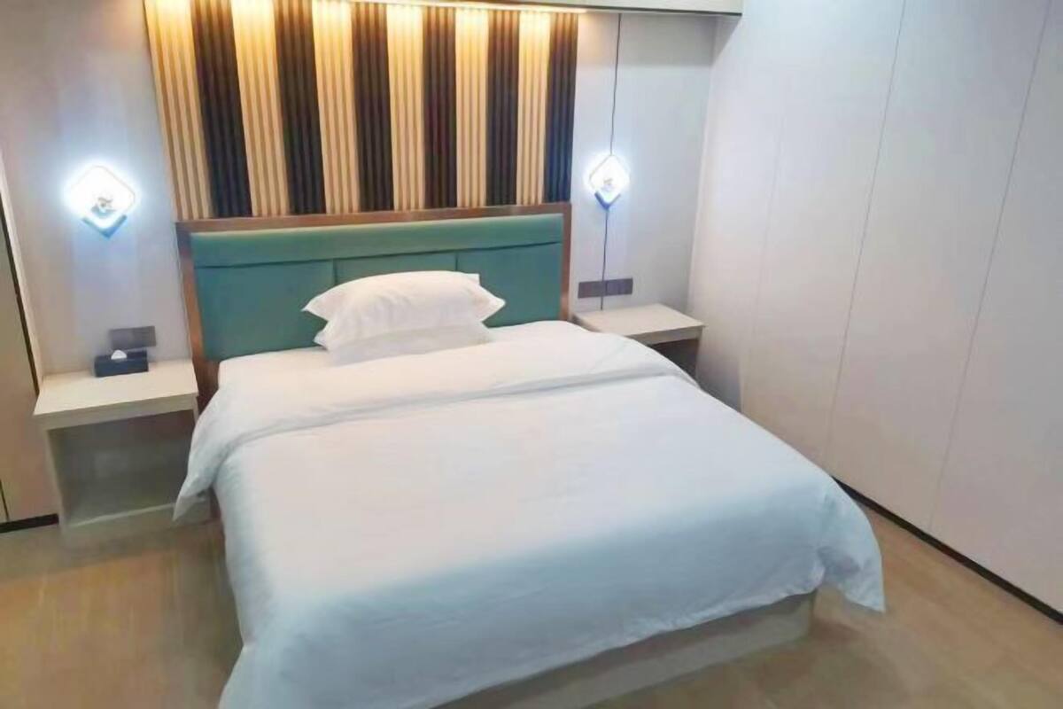 A hotel room with a bed, nightstands, and a headboard with vertical blinds.