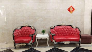 Deux fauteuils rouges à revêtement capitonné, ornés de motifs décoratifs, une petite table blanche avec une plante, et un symbole décoratif rouge sur le mur.