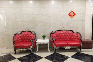 Two red upholstered chairs with ornate detailing, a small white table with a plant, and a red decorative symbol on the wall. - Huilong Hotel (Sihui)