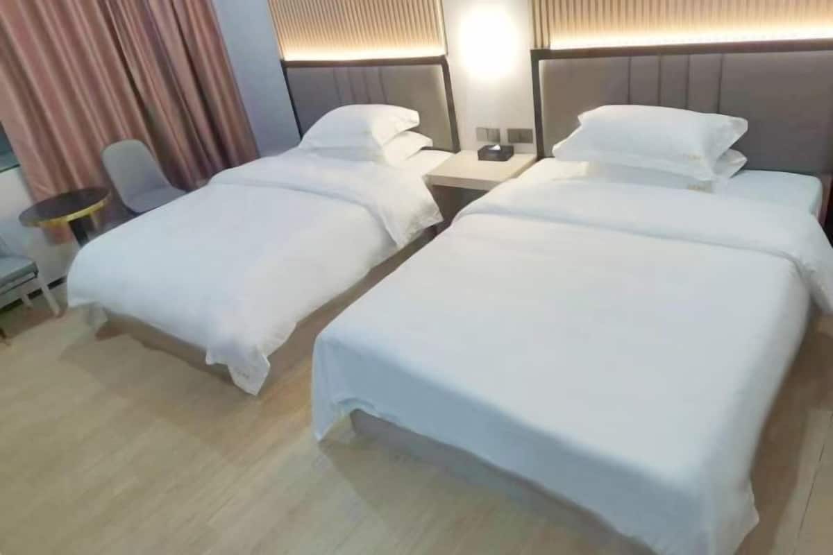 A hotel room with two single beds, a small table, a chair, and a bedside table with a lamp.