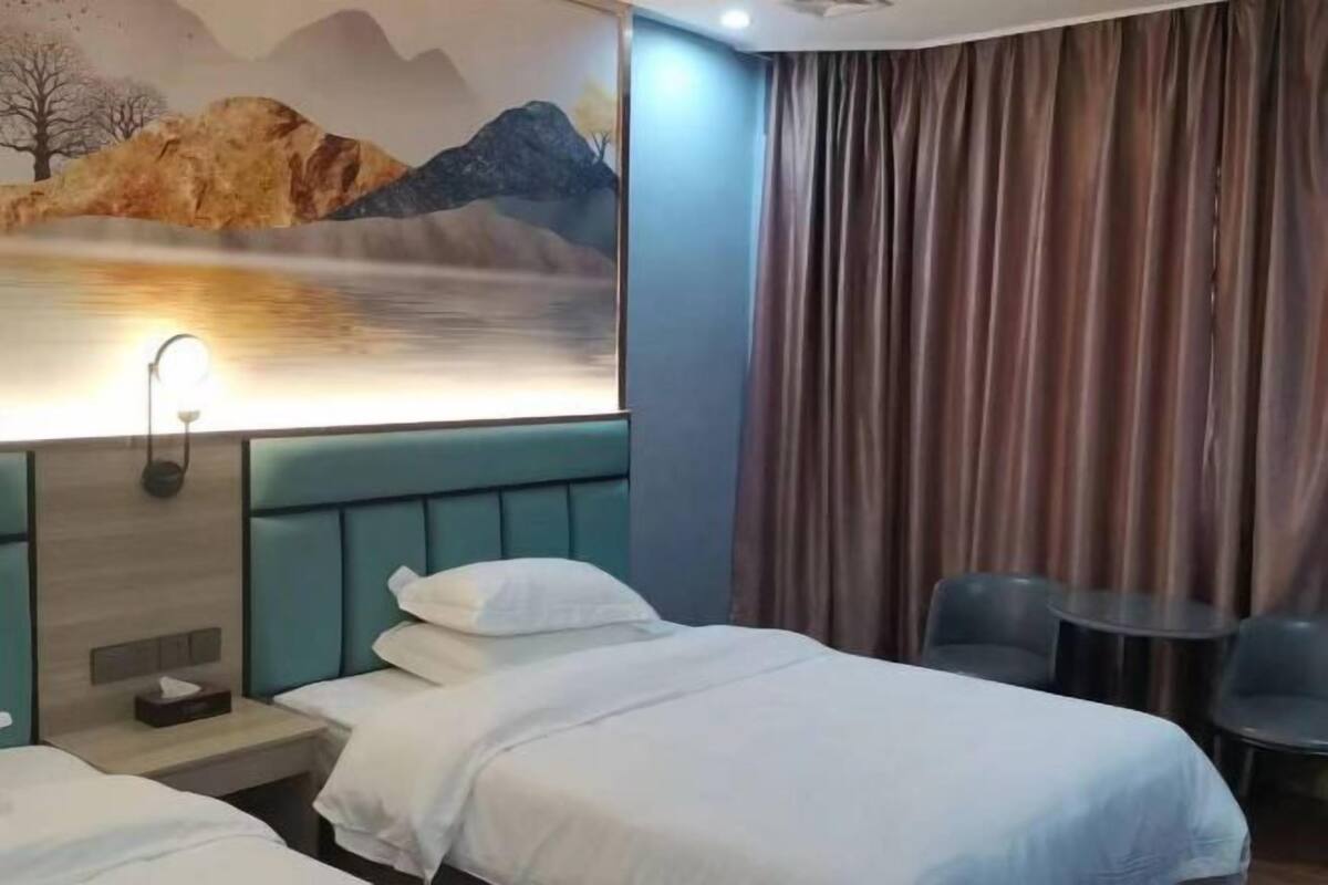 A hotel room with a bed, a nightstand, a wall-mounted lamp, and a painting of a landscape.