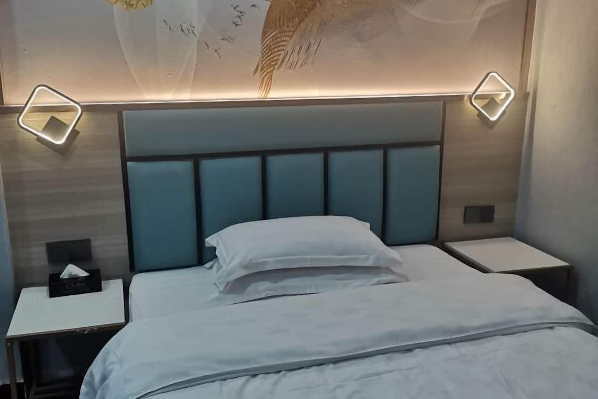 A hotel room with a bed, two bedside tables, and a wall-mounted light fixture.