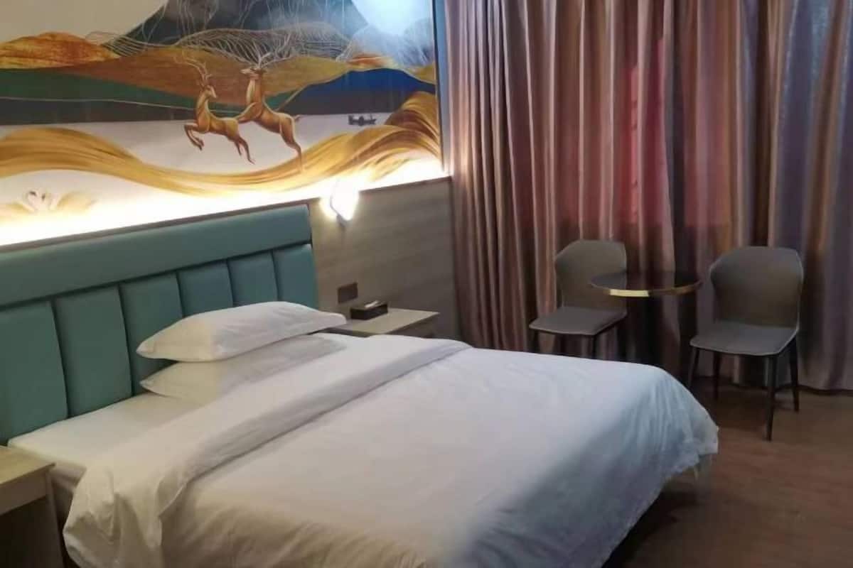 A hotel room with a large bed, two chairs, a small table, and a mural on the wall.