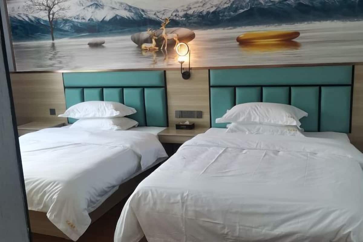 A hotel room with two beds, a mural of a mountain landscape, and a nightstand with a lamp.