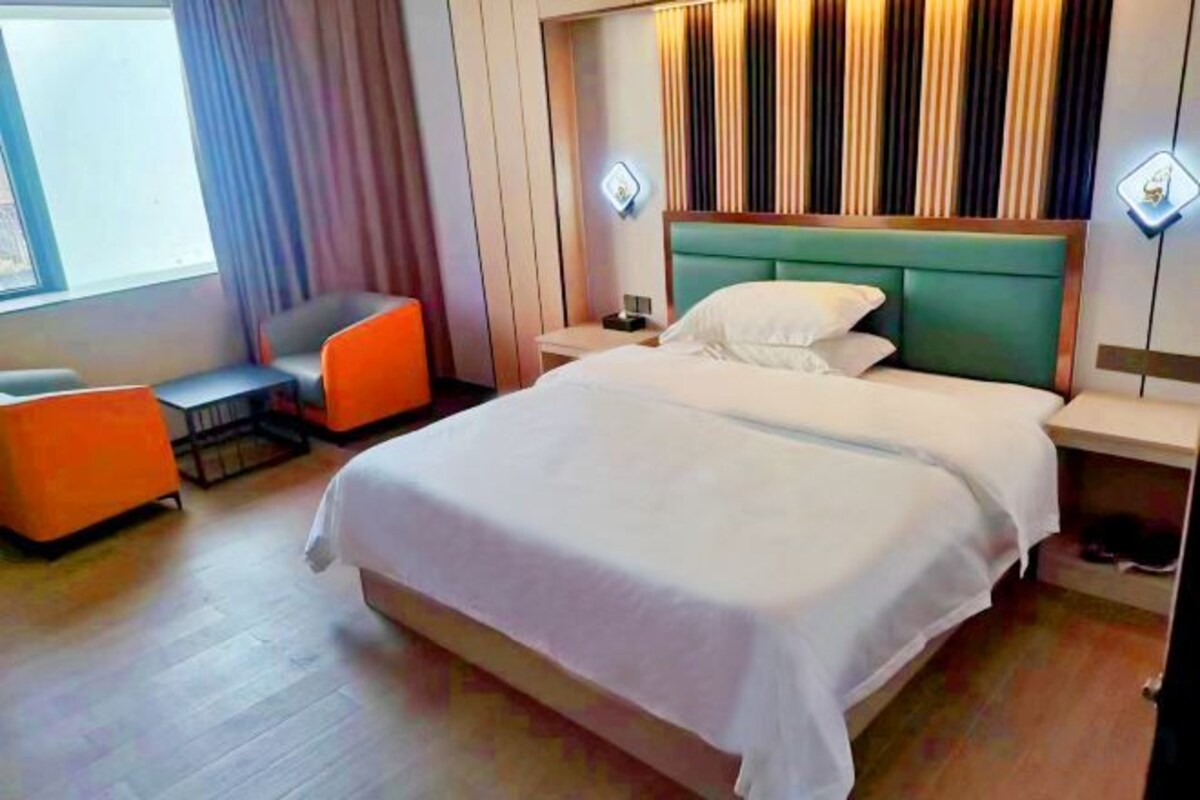 A hotel room with a large bed, a desk with a chair, and a window with curtains.