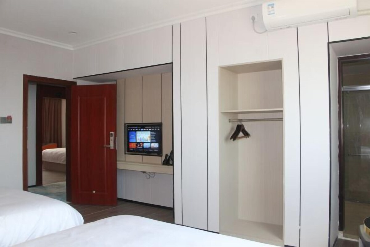 A hotel room with a bed, a TV, a wardrobe, and a door leading to another room.