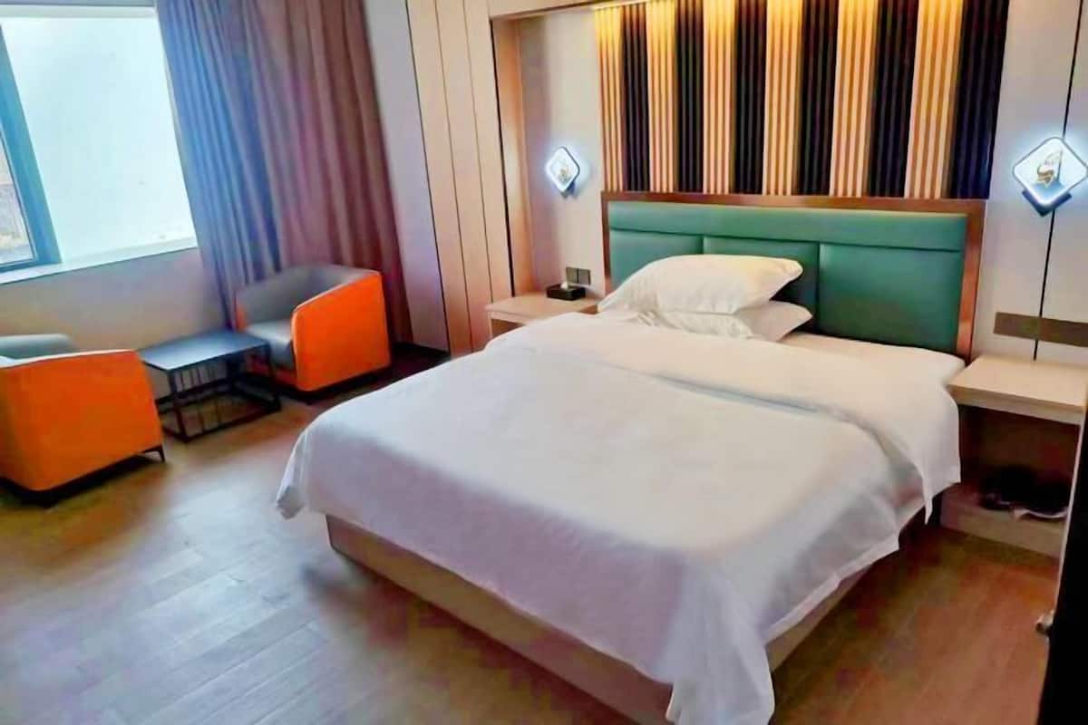 A hotel room with a large bed, a small table, an orange chair, and a nightstand.