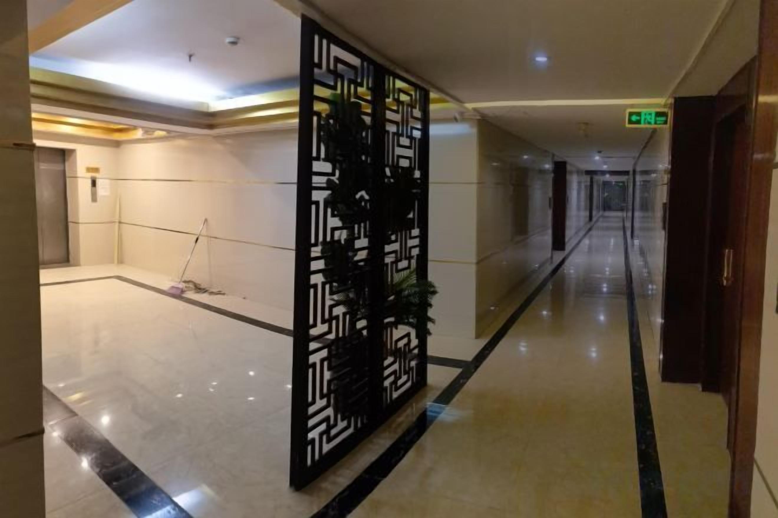 A hotel corridor with a decorative black panel, a polished floor, and a visible exit sign.