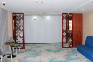 A room with a blue sofa, a small round table, and a chair. There is a patterned wall divider and a plain wall with a door. - Huilong Hotel (Sihui)