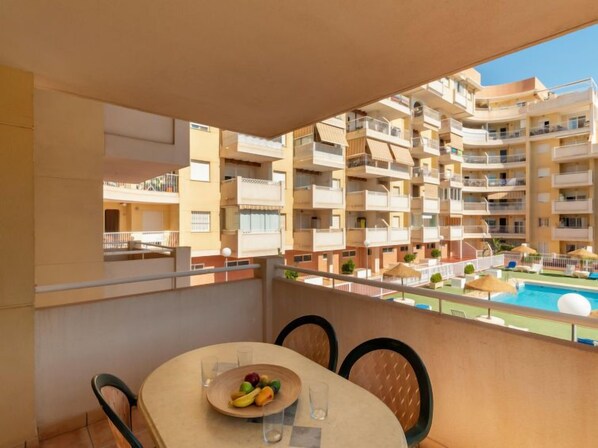 A balcony with a table set for two, overlooking a pool and a multi-story building with balconies.