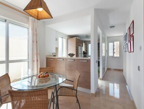 Una cocina moderna con armarios de madera, una mesa de comedor de vidrio, sillas de mimbre y una lámpara colgante.