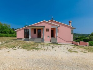 Une maison rose d’un seul étage, dotée d’un porche et d’une cheminée.