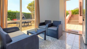 Uma sala de estar moderna com móveis de vime, grandes janelas e vista para um pátio.